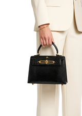 Black handbag held by a person wearing a beige suit on a white background