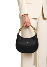 Black handbag with gold handle held by a person wearing a beige suit on a white background