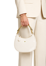 White handbag with gold handle held by a person wearing a beige suit.